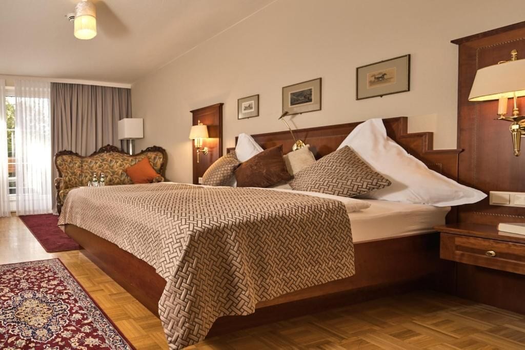 Una habitación de hotel con una cama grande, cabecero de madera y un tapete rojo estampado.
