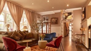 A modern living room with a sofa, two red chairs, a coffee table, and a large window with curtains. - Hotel Van Bebber (Xanten)