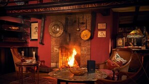 A cozy room with a fireplace, wooden furniture, and a red wall with framed pictures. - Hotel Van Bebber (Xanten)