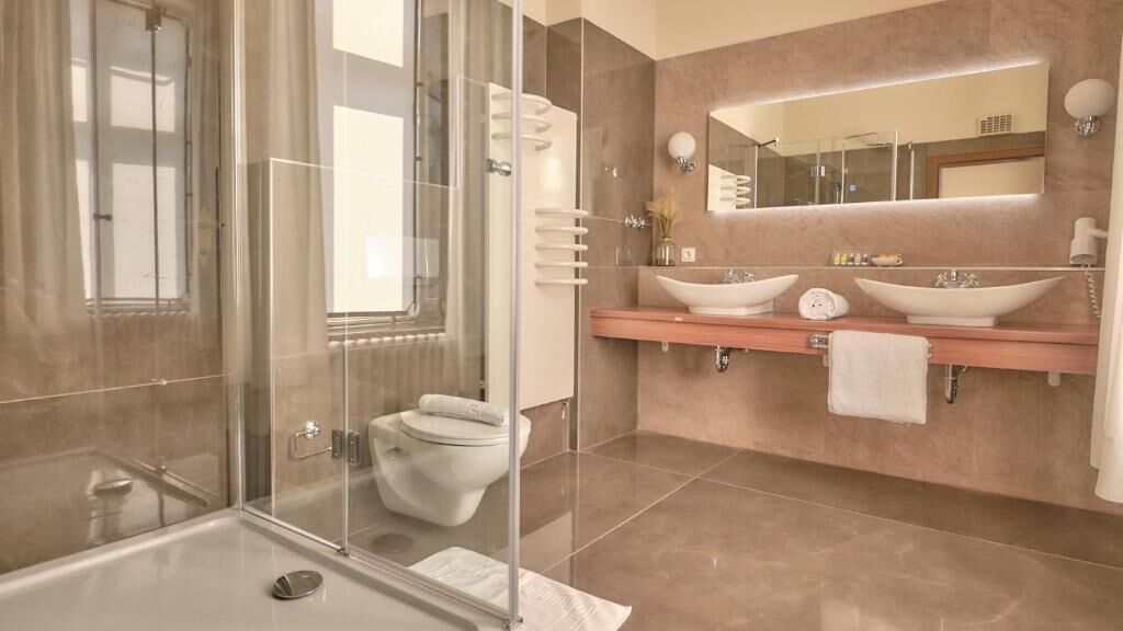 Ein modernes Badezimmer mit einer Duschkabine, einer Toilette und zwei Waschbecken mit Spiegel darüber.