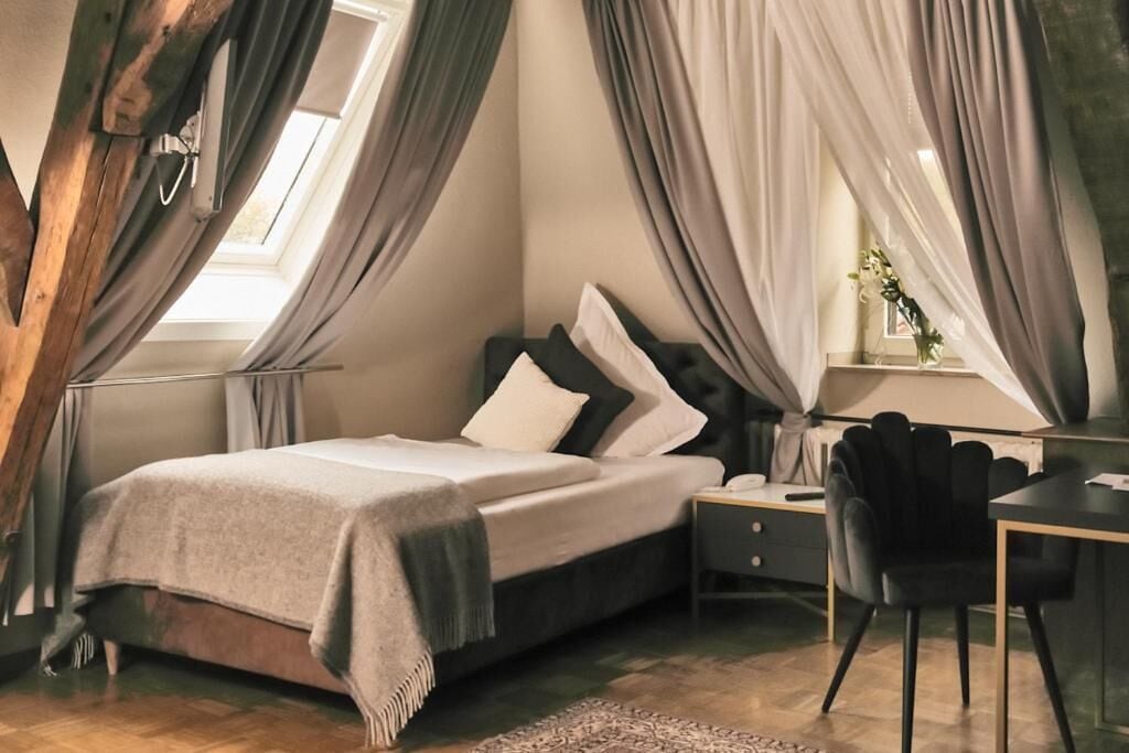 Un dormitorio con cama, mesita de noche, silla y cortinas.