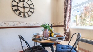 Un comedor con una mesa redonda, dos sillas, un reloj de pared y una ventana con cortinas.