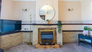 Una sala de estar con chimenea, televisor y un espejo en la pared.