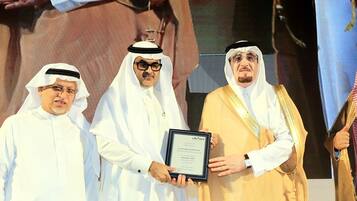 Three individuals in traditional attire holding a framed certificate.
