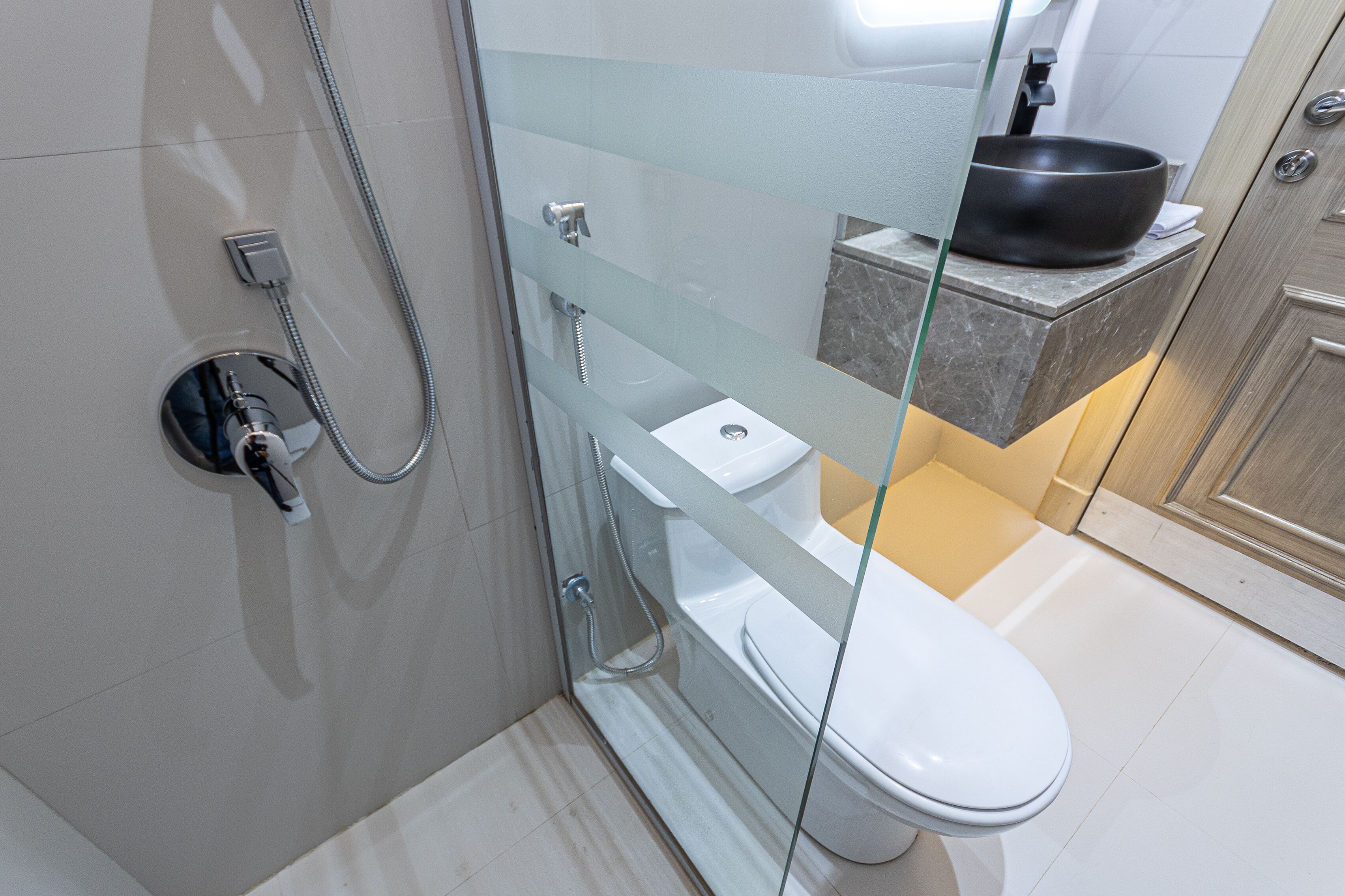 A modern bathroom with a glass shower enclosure, a white toilet, and a black basin on a marble countertop.