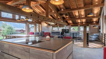 Un'ampia cucina con isola centrale, travi in legno a soffitto e lampade a sospensione, e ampie finestre che offrono vista sulla campagna circostante.