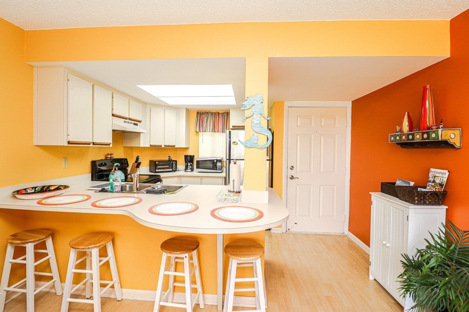 A compact kitchen with a central island, white cabinets, and a bright orange wall.