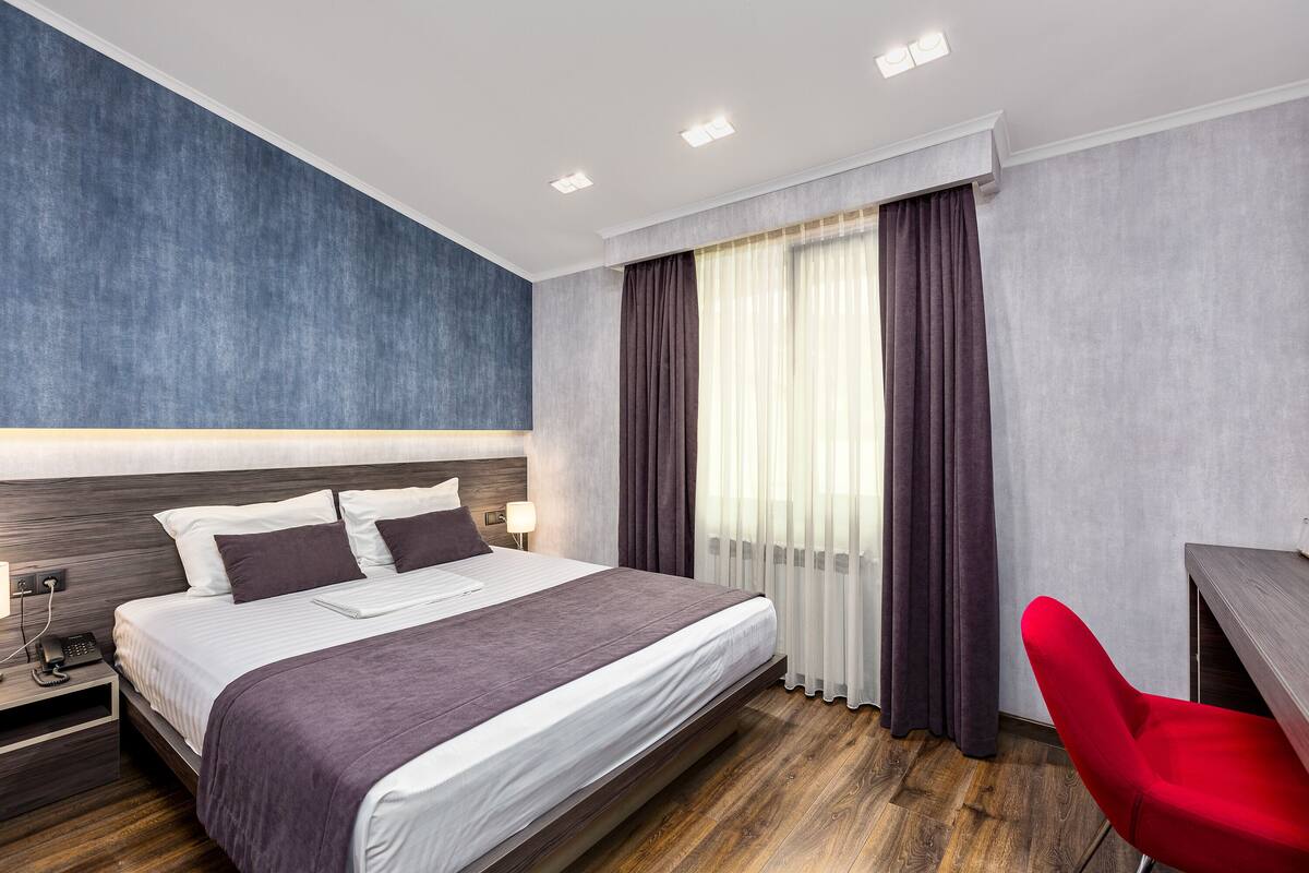 A modern hotel room with a large bed, a desk, and a red chair.