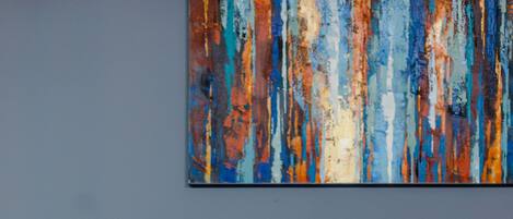A tufted leather sofa with wooden legs against a blue wall, with a colorful abstract painting above it.
