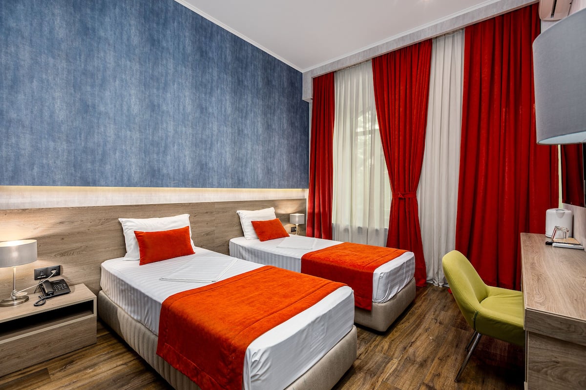 A hotel room with two beds, red and white curtains, a desk, and a chair.