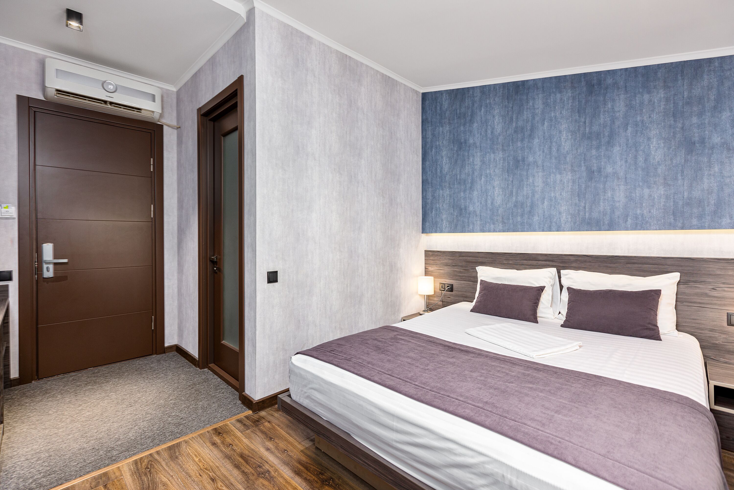 A hotel room with a bed, a desk, and an air conditioning unit.
