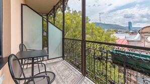 Un balcon avec une table et des chaises, une vue sur des immeubles et des arbres, et une rambarde en métal.