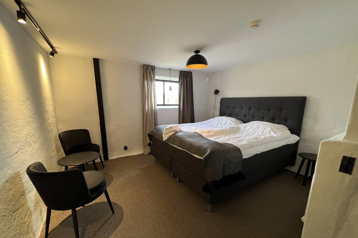 A hotel room with a large bed, a small desk, a chair, and a window with curtains.