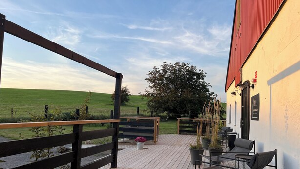 Una terraza de madera con mobiliario exterior y vista a un campo verde.