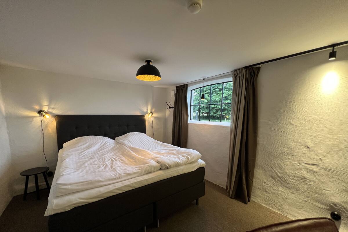 A bedroom with a bed, a nightstand, a chair, and a window with curtains.