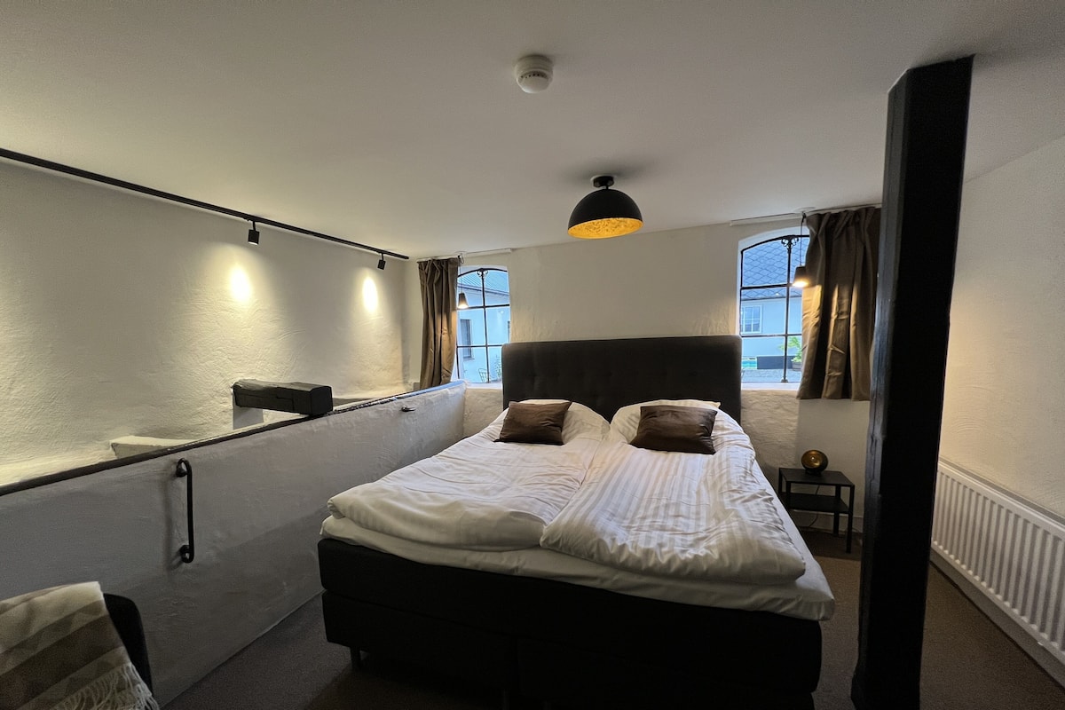 A hotel room with a large bed, a bedside table, a mirror, and a window with curtains.