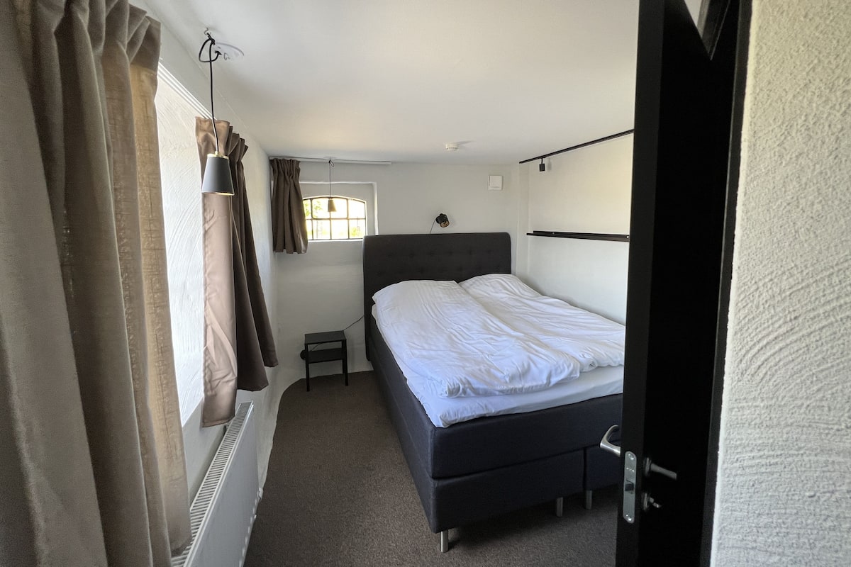A bedroom with a bed, a window, a nightstand, and a radiator.