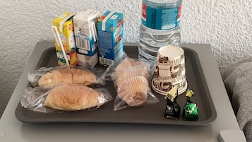Un refrigerador con una bandeja que contiene una botella de agua, cartones de jugo, pan y pequeños chocolates.