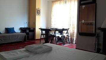 Une chambre d’hôtel avec un lit, un bureau et une chaise. Il y a une fenêtre avec des rideaux, une horloge murale et un tableau encadré.