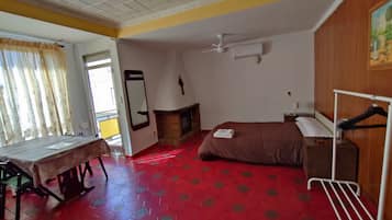 Ein Hotelzimmer mit einem Bett, einem Tisch, einem Spiegel, einem Deckenventilator und einem roten, gemusterten Boden.