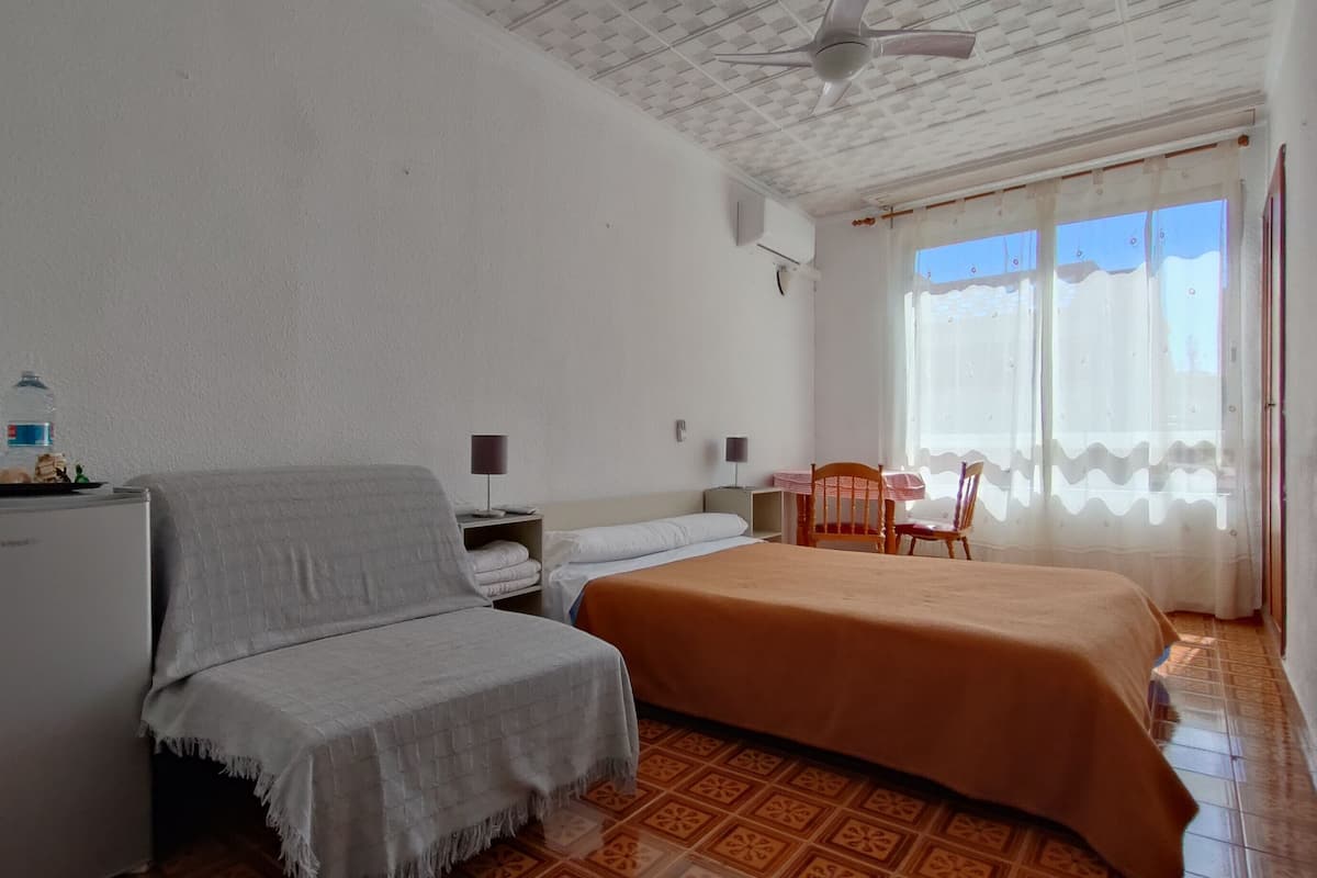 A hotel room with a bed, a sofa, a small table, and a refrigerator.