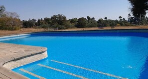 A clear blue swimming pool with a wooden deck and a stone border. - Brondesbury Park Hotel (Juliasdale)