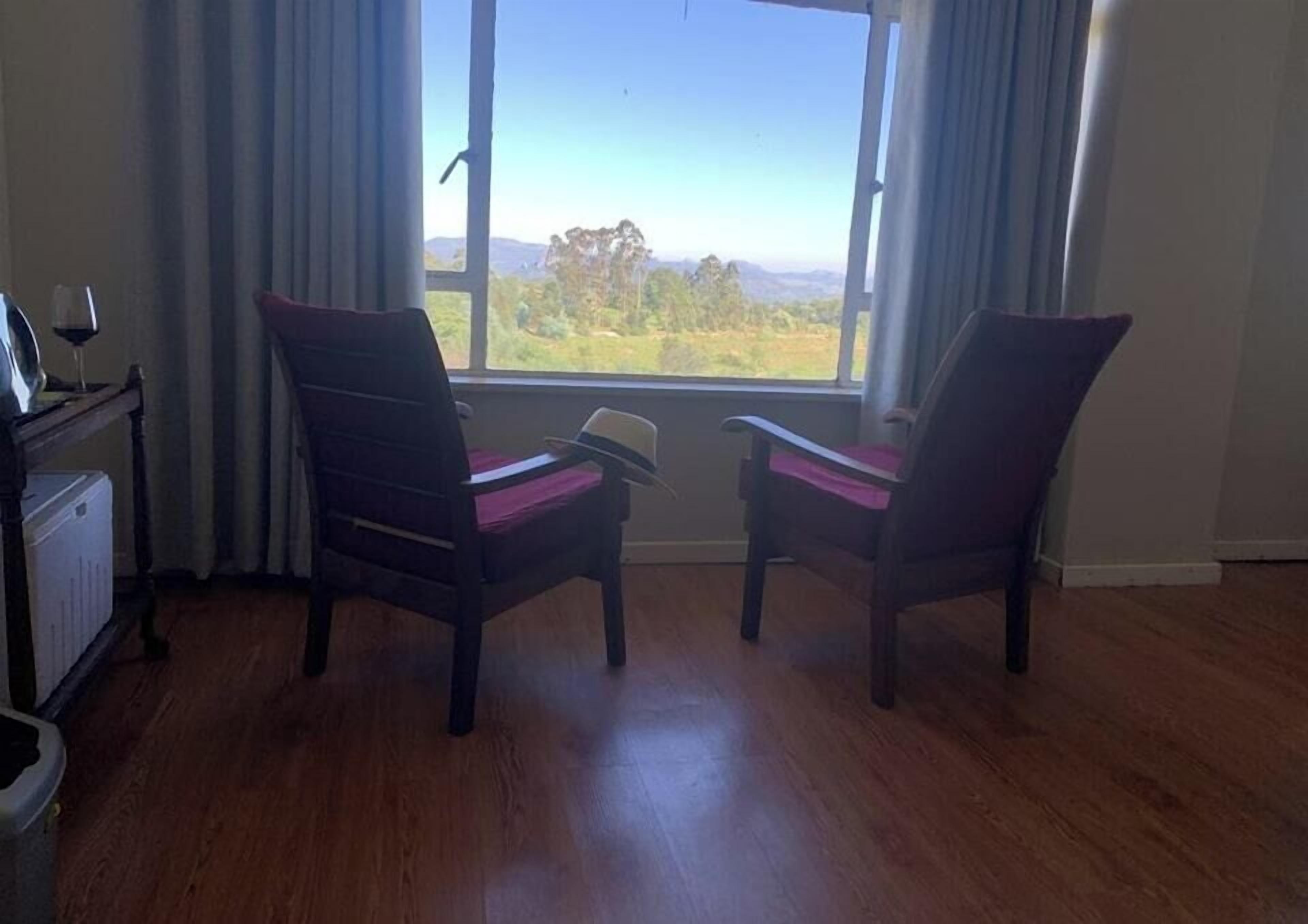 A room with two chairs facing a window with a view of a green landscape.