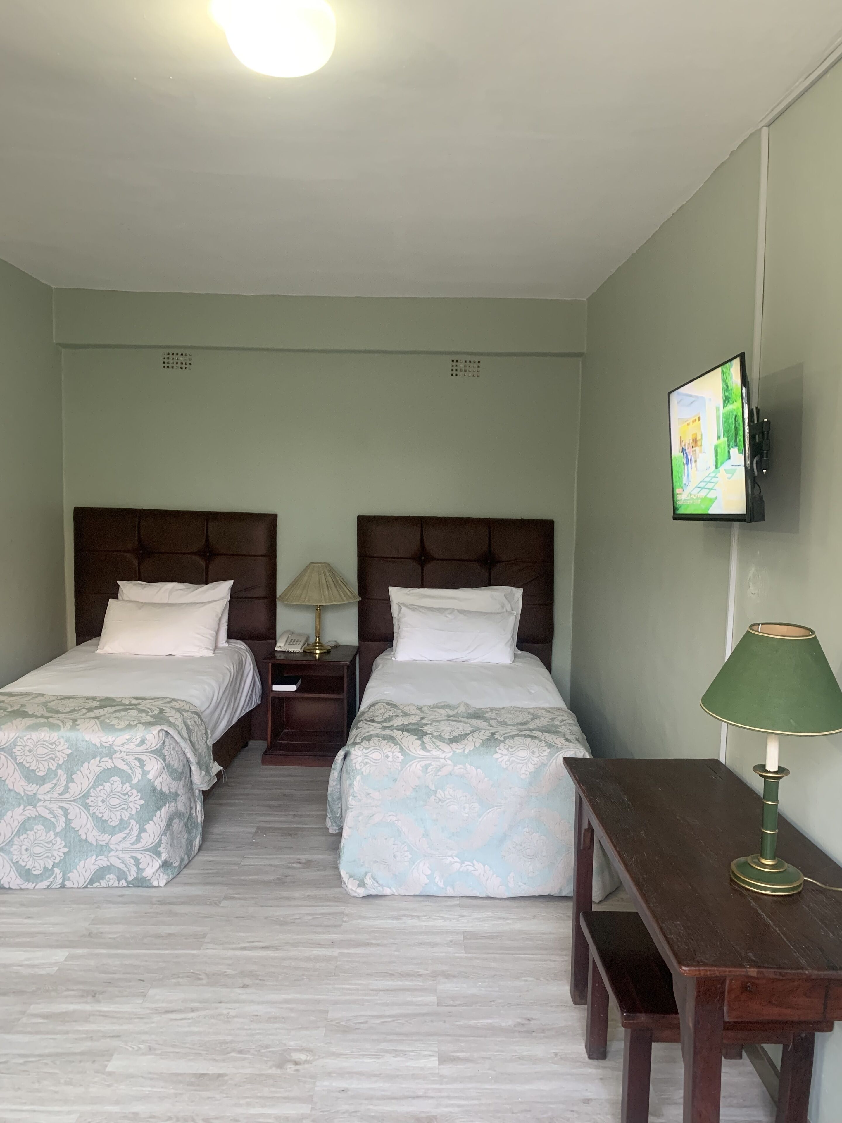 A hotel room with two beds, a desk, a chair, a TV mounted on the wall, and a lamp.