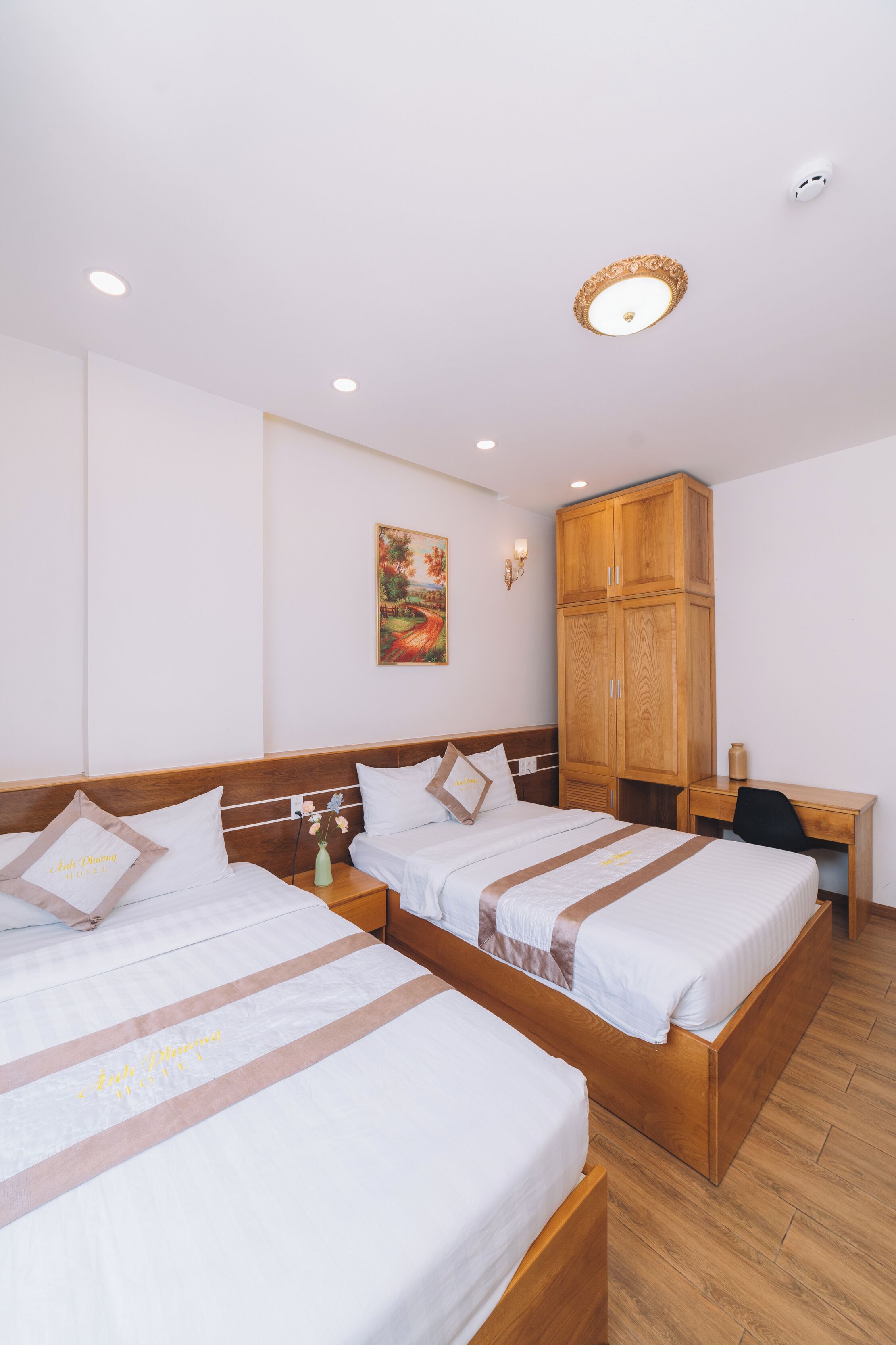 Una habitación de hotel con dos camas individuales, un armario de madera, un escritorio y un cuadro en la pared.