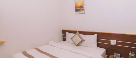 A neatly arranged hotel room with a wooden bed, a bedside table with a phone and toiletries, and a wall-mounted light fixture.