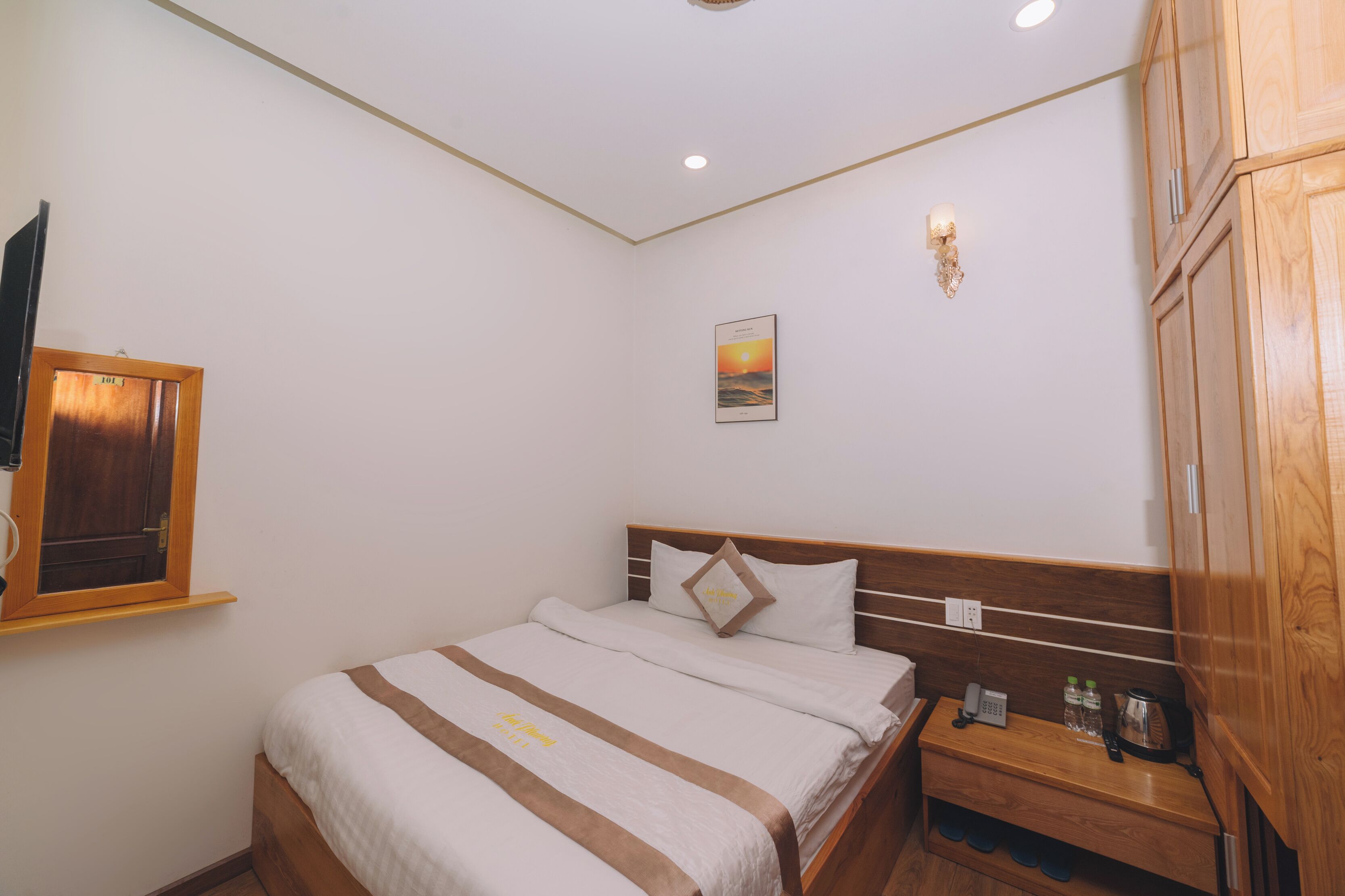 A neatly made bed with a striped bedspread, a bedside table with a phone and a kettle, and a wall-mounted light fixture.