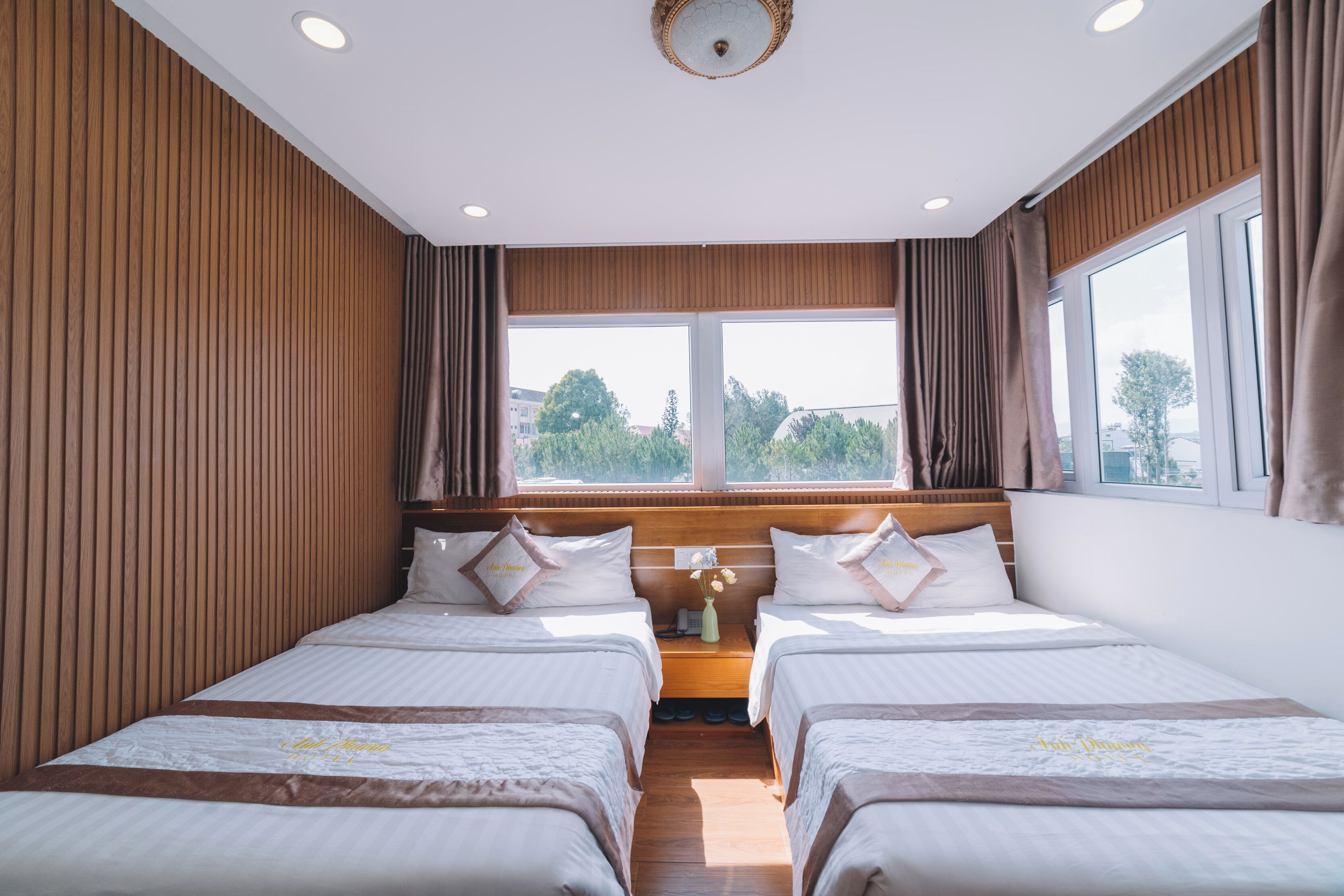 Ett hotellrum med två sängar, träpanel på väggarna, ett stort fönster och utsikt över träd.