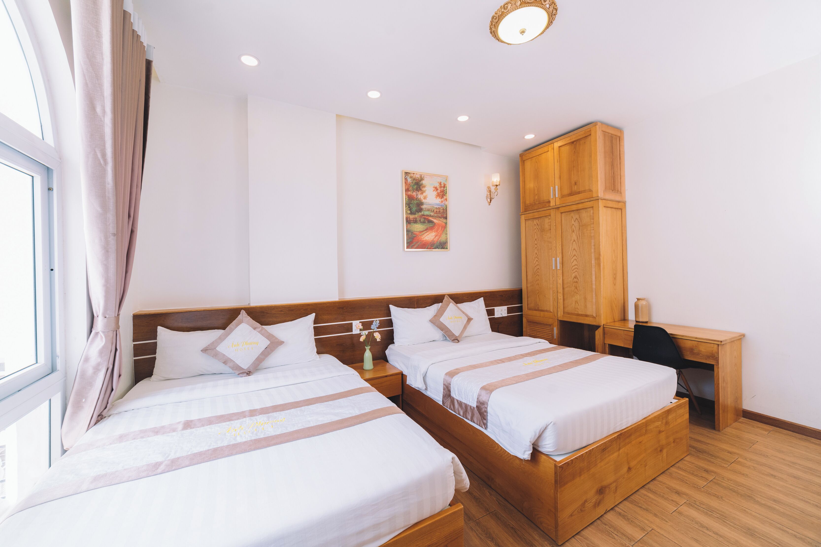 Habitación de hotel con dos camas, un armario de madera, un escritorio y un cuadro en la pared.