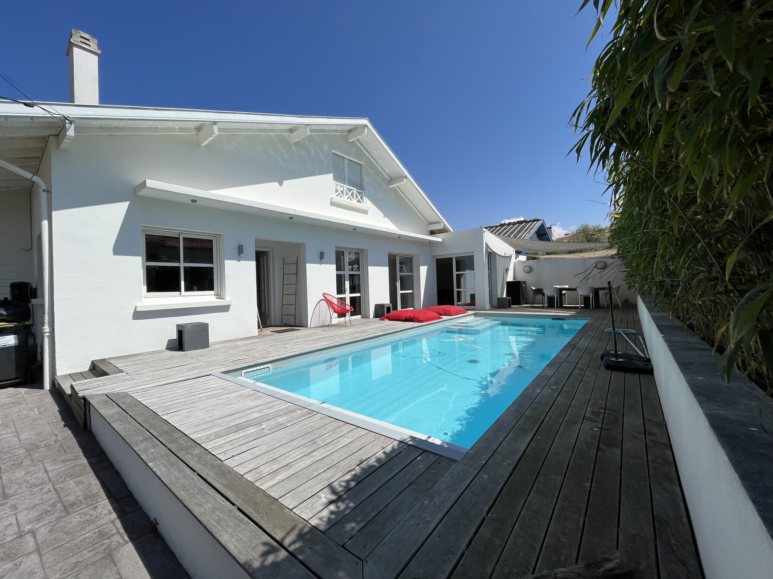 A modern house with a swimming pool, wooden deck, and red outdoor furniture.