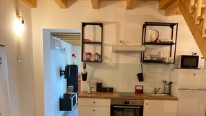 A compact kitchen with a dining area, wooden beams on the ceiling, and a microwave on the counter. - Cassiopeia House (Porto Palo)