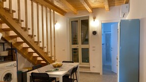 A kitchen with a wooden staircase, a dining table with chairs, a washing machine, and a refrigerator. - Cassiopeia House (Porto Palo)