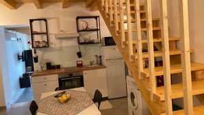 A compact kitchen with a dining area, wooden staircase, and a washing machine. - Cassiopeia House (Porto Palo)