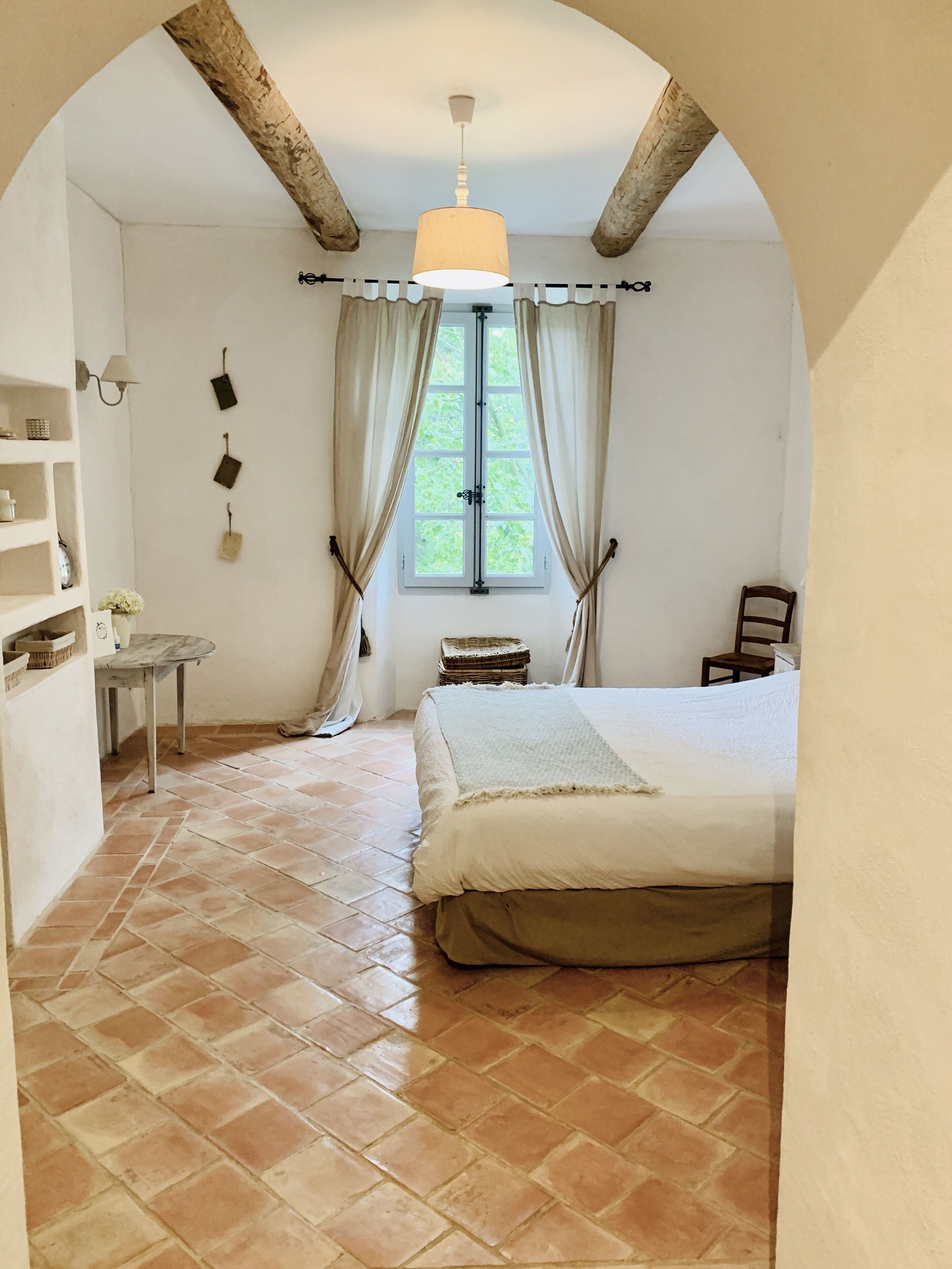 Una camera da letto con un letto grande, un tavolino, una sedia, una finestra con tende e un soffitto in legno.