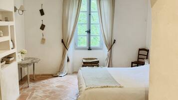 Una camera da letto con un letto grande, un tavolino, una sedia, una finestra con tende e un soffitto in legno.