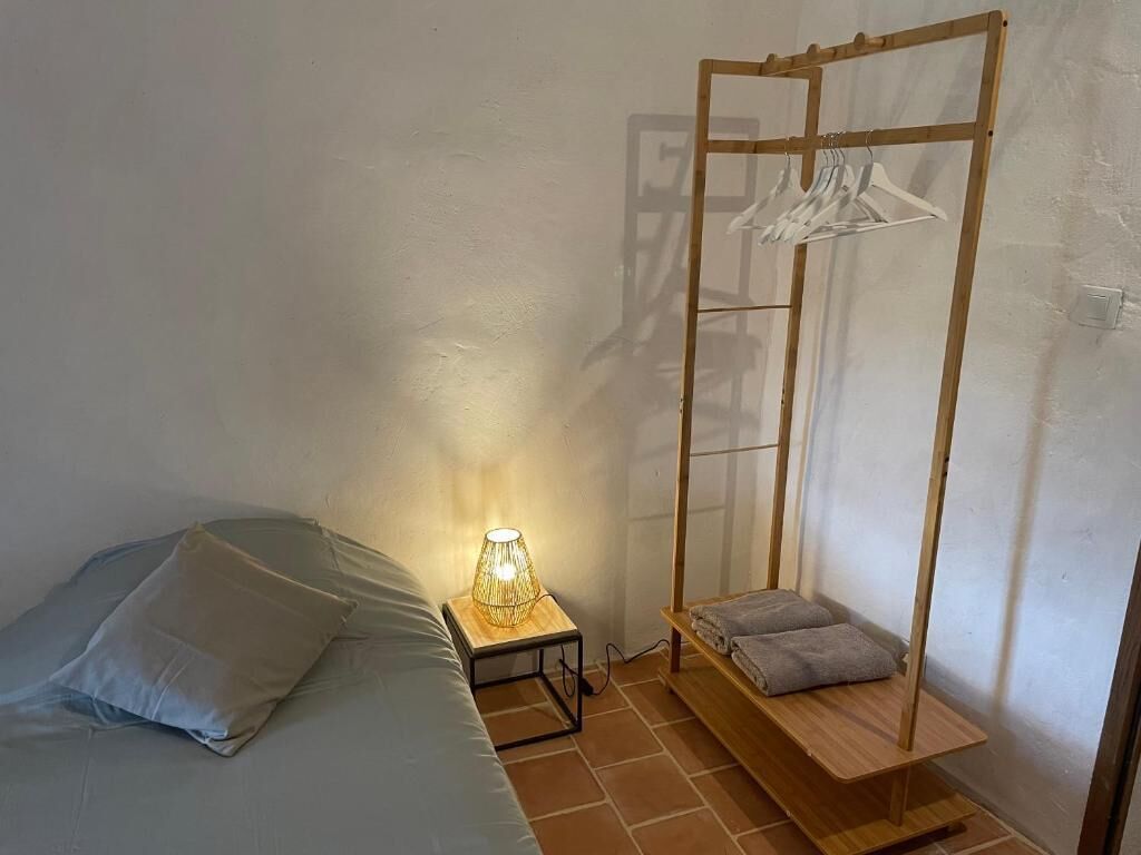 A bedroom with a bed, a bedside table with a lamp, a wooden swing chair, and a clothing rack.