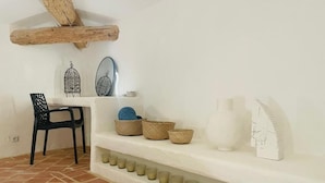 A room with a white wall, a black chair, a shelf with baskets and a white vase, and a tiled floor. - La Bastide (Saint-Julien)