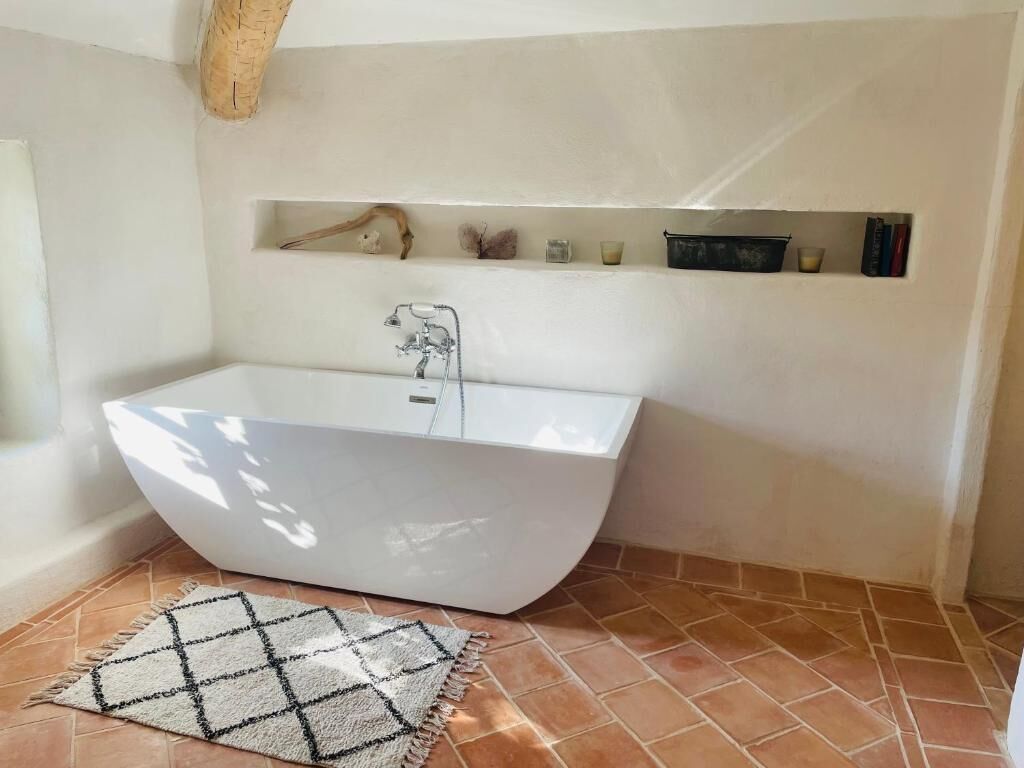 Une salle de bain moderne avec une baignoire sur pieds, une étagère ornée d’objets décoratifs et un tapis à motifs.