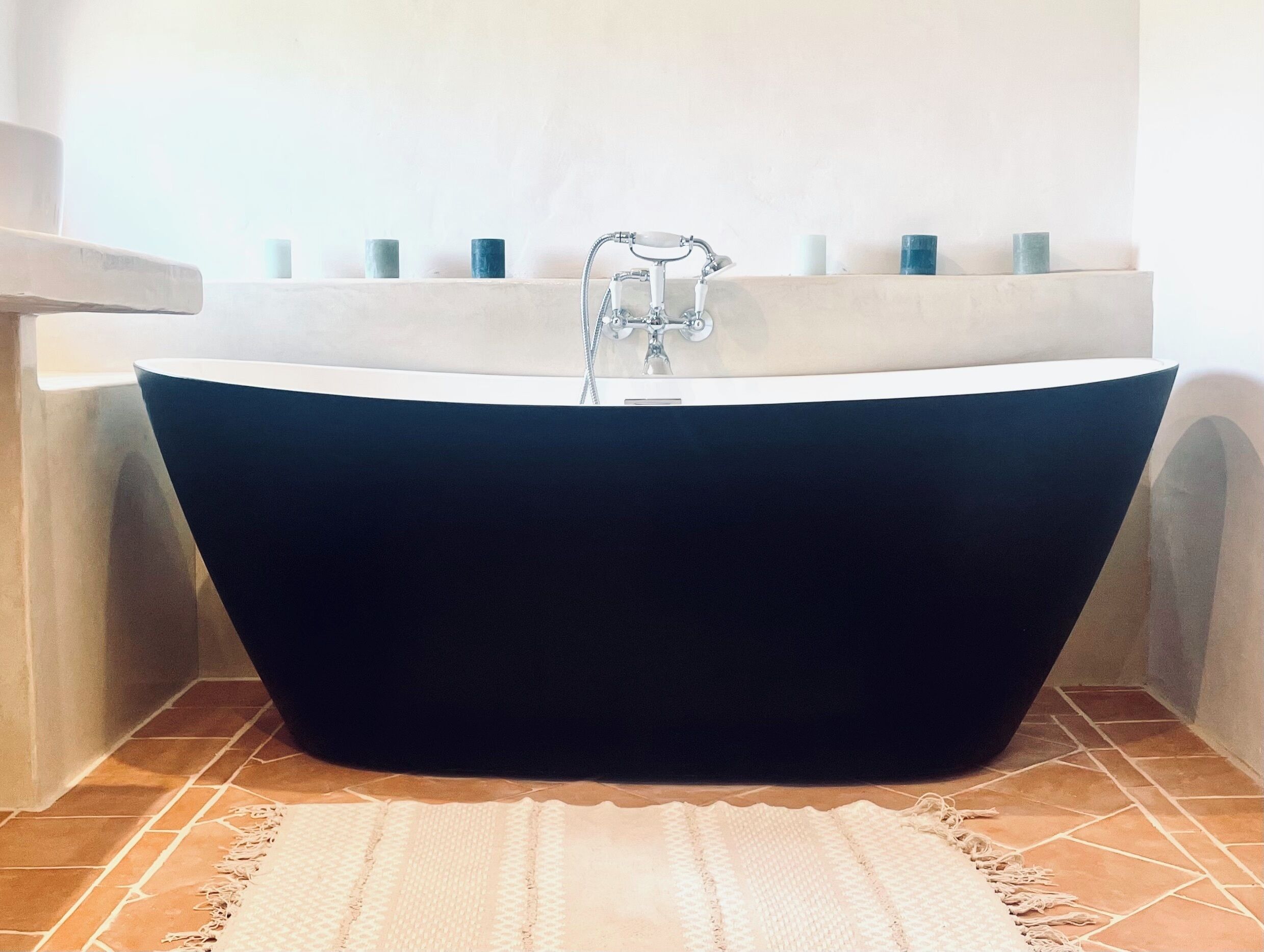 Una vasca da bagno indipendente in un bagno con pavimento piastrellato e tappeto bianco.