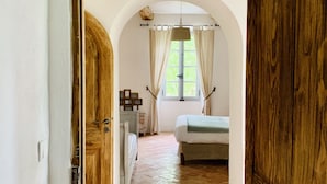 A bedroom with a bed, a window with curtains, a wooden door, and a tiled floor. - La Bastide (Saint-Julien)