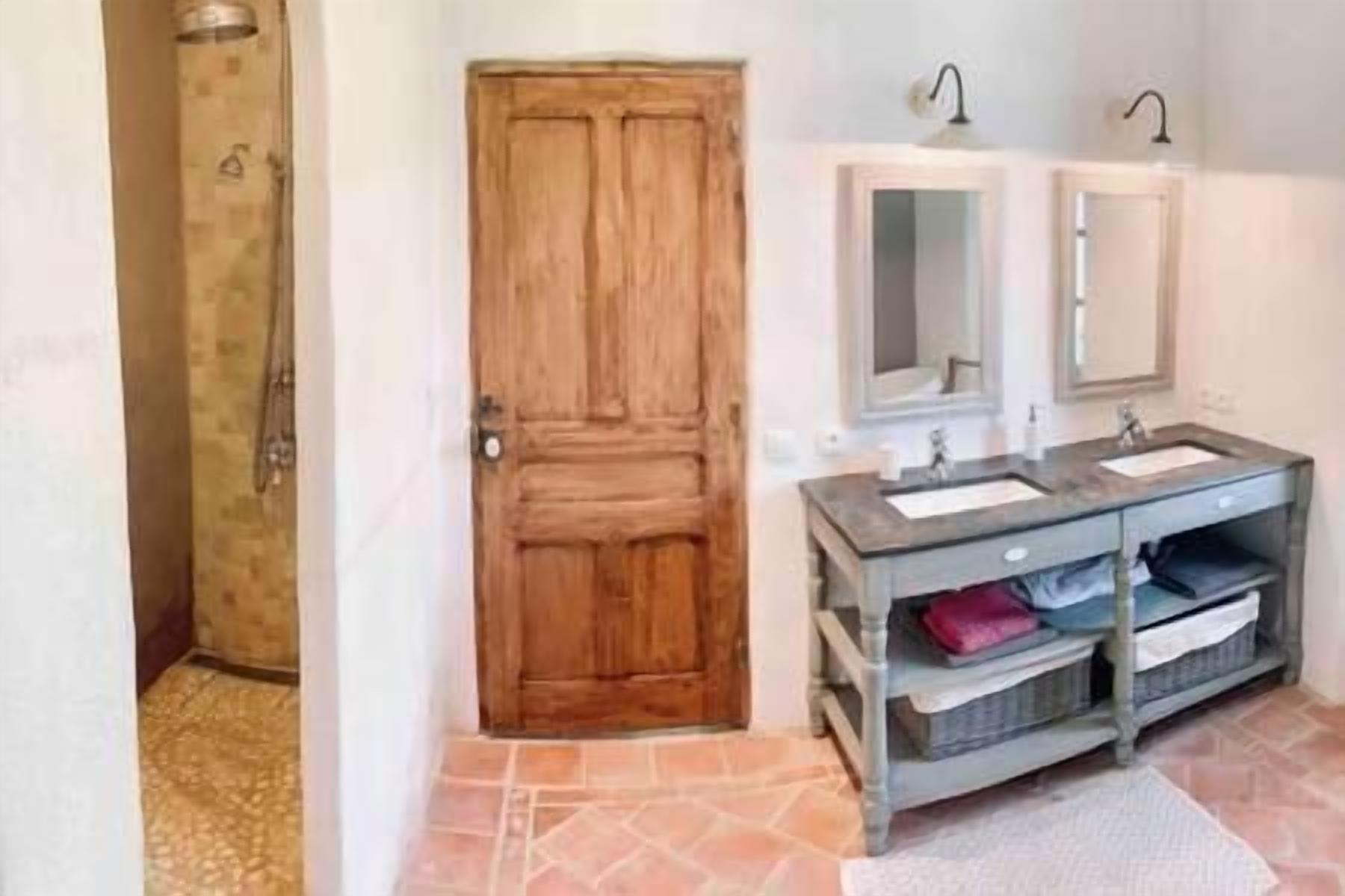A bathroom with a wooden door, two mirrors above a sink, and a tiled floor.