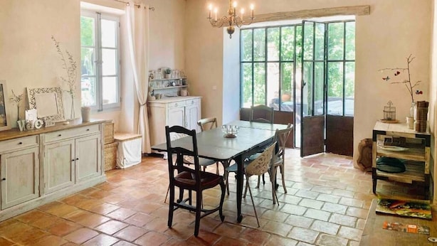 A rustic dining area with a wooden table and chairs, a chandelier, and a view through large windows. - La Bastide (Saint-Julien)