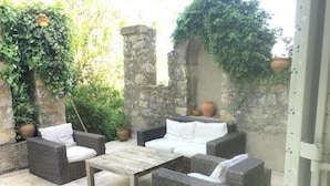 An outdoor patio with wicker furniture, a stone wall, and potted plants. - La Bastide (Saint-Julien)