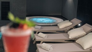 Een wellnessruimte met een bubbelbad, loungezetels en een drankje.