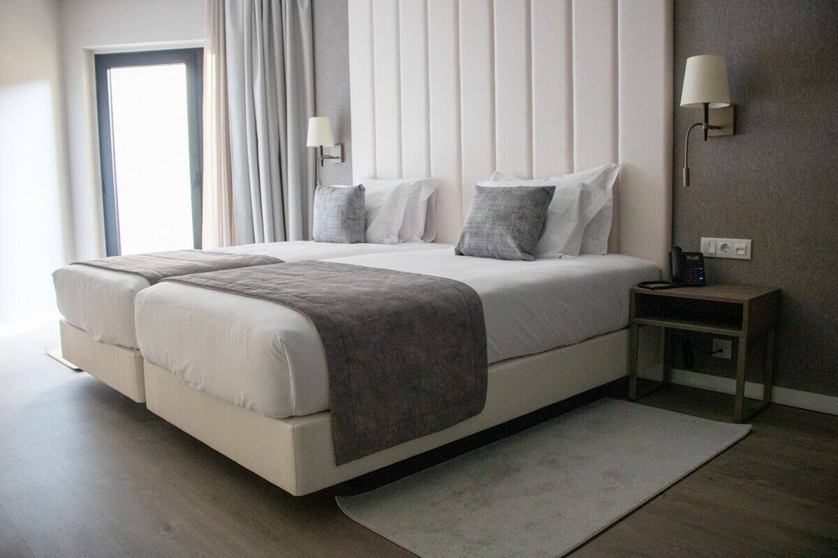 Habitación de hotel moderna con una cama grande, una mesita de noche, una lámpara y vistas al exterior.