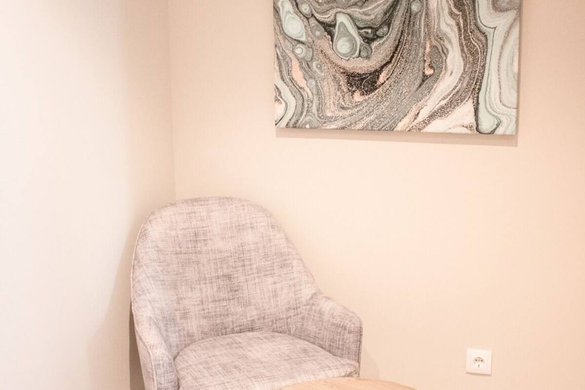 Una habitación con un sillón gris y una pequeña mesa de madera frente a una pared con un cuadro abstracto grande.